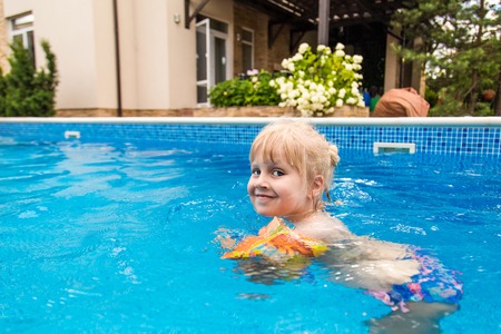 Little cute blonde girl swimming in a pool , wearing inflatable sleeves.  She is smiling and happyの写真素材