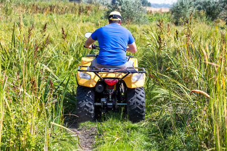 Caucasian man in sport protective goggles riding an ATV quad bike over rough terrain between high grass bushes. Adventure activity conceptの写真素材