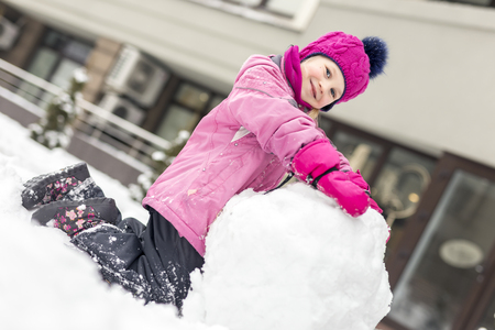 Portrait of cute little girl making smowman. at bright winter day. Adorable child playing with snow outdoors. Funny winter activities for kids and family.の写真素材