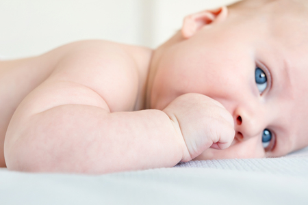 Portrait of infant kid lying on a bed. Close-up of healthy child sucking his fist. Focus on fist...