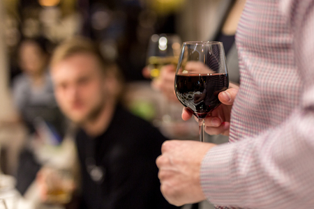 Adult hand holding glass of red whine. Toasting at celebration . Cafe or restaurant background.  Chief speech while corporate business party.の写真素材
