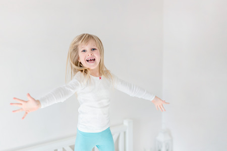 Happy kid jumping over bed. Cute little blond girl having fun indoors. Happy and careless childhood conceptの写真素材
