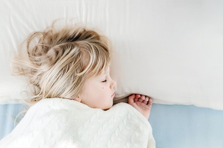 Little cute girl sleeping on pillow in bed. Kid covered with warm soft yarn knitted blanket. Healthy daytime sleep conceptの写真素材