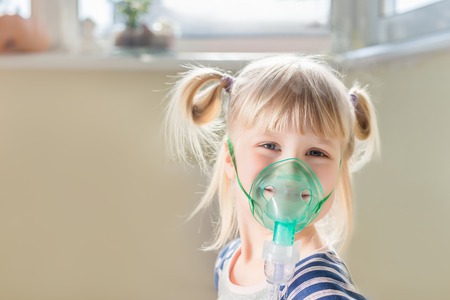 Happy smiling kid using nebuliser mask. Inhalation therapy curing chest cold and coughing. Healthcare and disease prevention conceptの写真素材