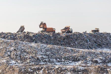 Dump trucks unloading garbage over vast landfill.  Environmental pollution. Outdated method of wasate disposal. Survival of times past.の写真素材
