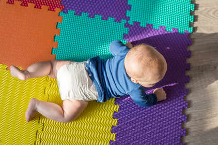Infant baby boy playing on colorful soft mat. Little child  making first crawling steps on floor. Top view from aboveの写真素材