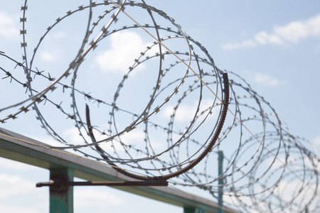 Fence with razor barbed wire protection against blue sky background. Dictatorship and tyranny conceptの写真素材