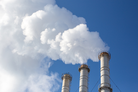 Smoking pipes making clouds against blue sky background. Dioxide air contamination. Environmental pollution.の写真素材