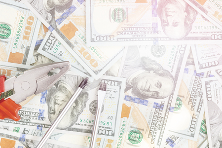 Tools lying over 100 dollars banknotes background. Pliers and screwdriver against US money. Correction, fixing and improvement of budget concept. Copyspace.の写真素材