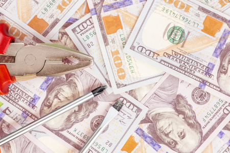 Tools lying over 100 dollars banknotes background. Pliers and screwdriver against US money. Correction, adjustment and improvement of budget and finance concept. Toned. Copyspace.の写真素材