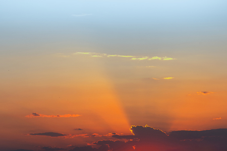 Dramatic sunset sky. Fiery bright colors of sun going down. Sunlight rays shining from behind clouds. Scenic nature backgroundの写真素材
