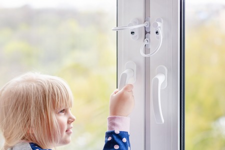 Little cute toddler girl trying to open window in apartment at high-tower building. Children window...