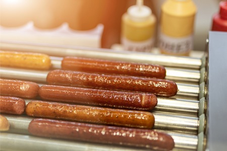Close-up sausages frying on electric grill. Automatic barbeque for fast food hot-dog snack.の写真素材