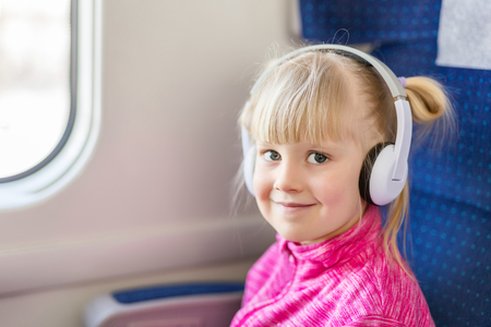 Little cute girl travelling by train. Kid listening to music with white headphones. Children activity and entertainment during trip conceptの写真素材