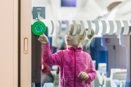 Little girl in modern passenger trail. Kid standing at gangway and touching button to open...