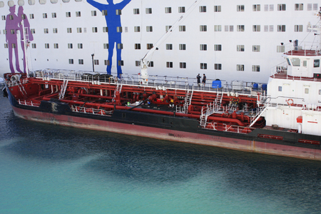 Delivering ship refueling big white passenger cruise liner. Refueling of heavy commercial ship in water at harbor.の写真素材