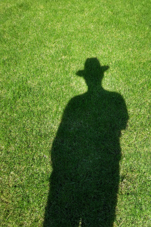 Shadow silhouette of man wearing hat on green grass lawn. Human shade on fresh natural meadow.の写真素材