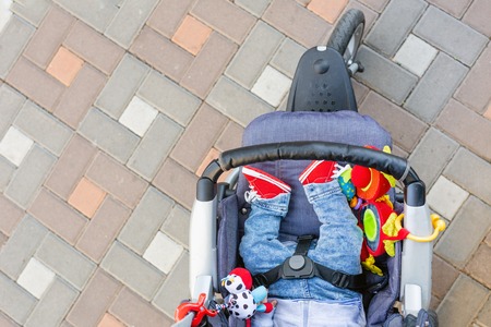 Baby sleeping three-wheel stroller outdoor. Child in bright casual costume lying at big comfortable pram. Parent walking with carriage in city park. View from above.の写真素材