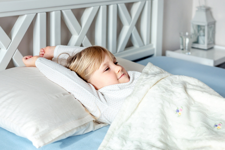 Cute little blond caucasian girl awakening at bed in morning. Child wake up early to go to school. Stretching and yawning. Healthy sleeping. Children healthcareの写真素材