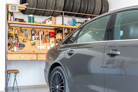 Luxury car parked at large spacious private home garage. Big wooden workbench with lot of tools at background. Spare season wheels storage. DIY, self service and repairの写真素材