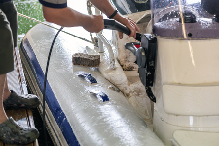 Man washing white inflatable boat with brush and pressure water system at garage. Ship service and seasonal maintenance concept.の写真素材