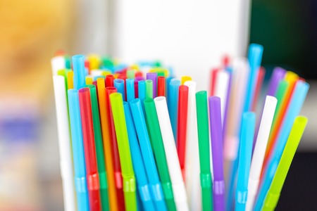 Bunch of colorful plastic sipping straws in wooden box at cafe counter. Drinks decoration and accessories. Bright multicolored background.の写真素材