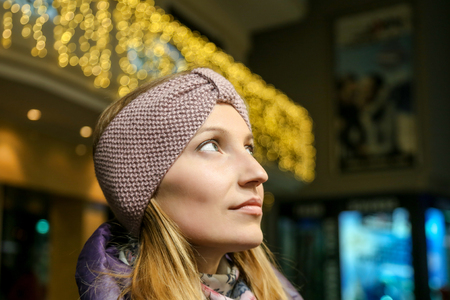 Portrait of young pretty woman in beautiful knitted woolen headband outdoors at cold autumn day. Evening bokeh lights on background. Handmade craft fashion clothes.の写真素材