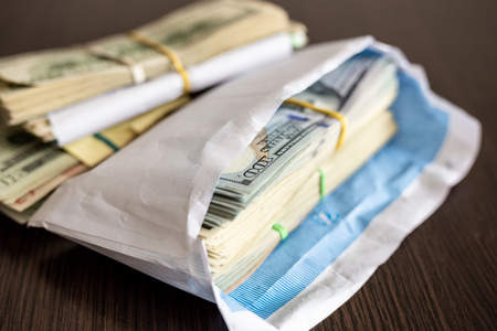 Bundle of american dollar banknotes in white envelope on wooden table. Secondary black economy concept. Envelope wages. Bribery and economical crime.の写真素材