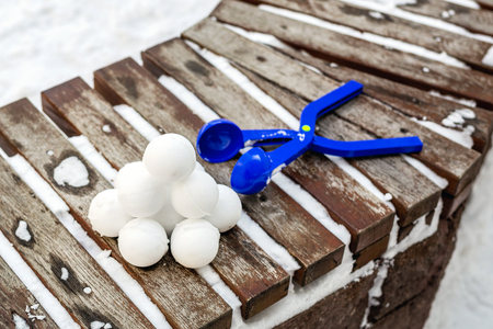 Blue plastic snowball maker tool with set of ready snowballs laying on a wooden bench near outdoor children playground at winter day.の写真素材