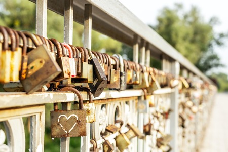 Many old rusty metal locks closed on fence of bridge over river. Love forever through time concept.の写真素材