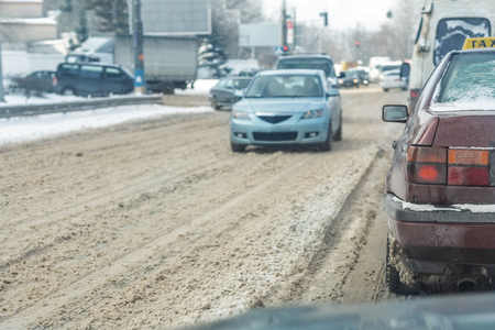 Cars moving on city street on slippery snowy road in winter. Vehicles covered with snow drift after snowfalls and blizzard at cold winter season. Weather forecast.の写真素材