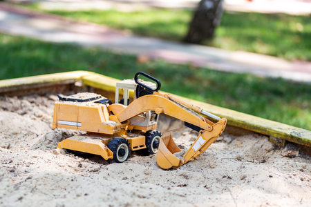 Yellow excavator toy in wooden sandbox at yard. Boy's toys concept.の写真素材