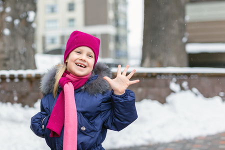 Portrait of happy adorable child laughing on city street during snowfall. Cute little caucasian girl in knitted hat and scarf and dawn jacket having fun playing outdoor in winter. Weather and seasons.の写真素材