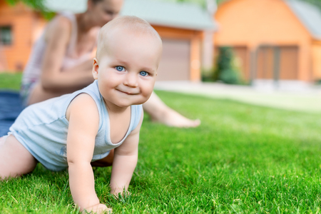 Portrait of cute little caucasian boy having fun in garden with mother. Child crawling on green grass lawn during walk with mom in yard. Happy childhood and baby healthcare.の写真素材