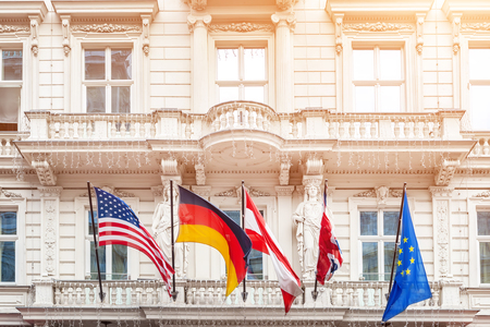 National flags on old building facade in european city. Flags of USA, Germany, Austria, European Union and folded Great Britain flag. Brexit concept.の写真素材