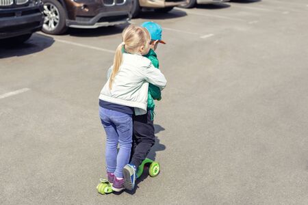 Two frineds boy and girl having fun riding one scooter together simultaneously. Children playing on car parking road. Danger and risk of accident.の写真素材