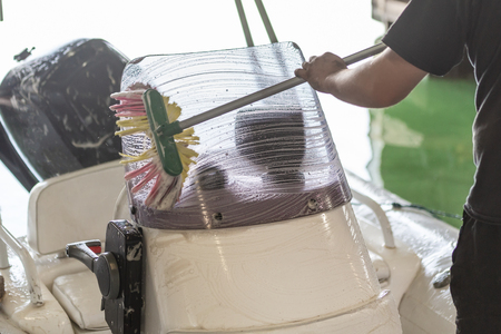 Man washing white inflatable boat with brush and pressure water system at garage. Ship service and seasonal maintenance conceptの写真素材