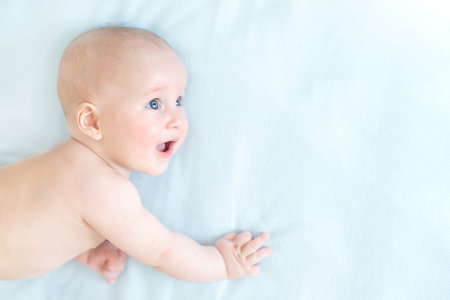 Profile portrait of cute little baby boy lying on blue blanket and looking aside. Child with open mouth and wide opened eyes. Astonished surprised kid. Copyspaceの写真素材