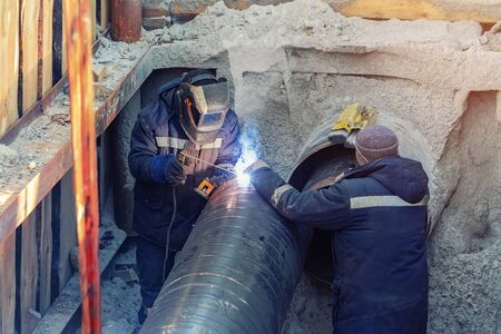 Welder welding water or gas steel pipeline with assistant worker in trench. City underground utilitites renewal and replacement,の写真素材