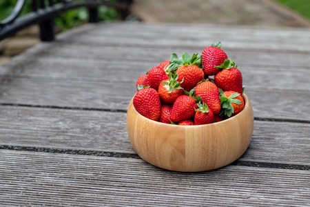 Sweet fresh juicy organic ripe strawberries in wooden bowl on wooden surface outdoors.