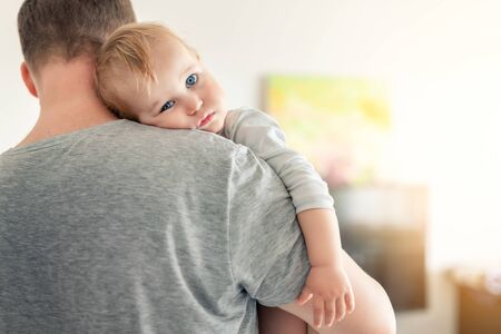 Close-up portrait of cute adorable blond caucasian toddler boy on fathers shoulder indoors. Sweet little child feeling safety on daddys hand. Responsibility and childcare. happy childhood.の写真素材
