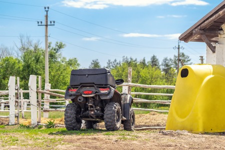 ATV quad bike vehicle standing near wooden fence at farm or horse stable. Back view of all wheel drive motorcycle at farm. Rural countryside machine.の写真素材
