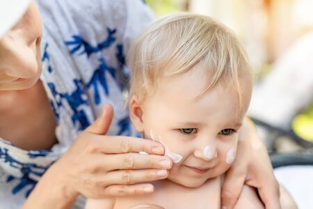 Mother applying sunscreen protection creme on cute little toddler boy face. Mom using sunblocking lotion to protect baby from sun during summer sea vacation. Children healthcare at travel time.の写真素材