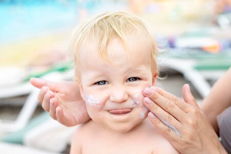 Mother applying sunscreen protection creme on cute little toddler boy face. Mom using sunblocking lotion to protect baby from sun during summer sea vacation. Children healthcare at travel time.の写真素材
