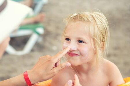 Mother applying sunscreen protection creme on cute little daughter face. Mom using sunblocking lotion to protect kid girl from sun during summer sea vacation. Children healthcare at travel time.の写真素材