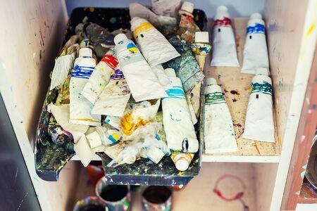 Heap of many different multicolored old dirty used oil paints tubes on shelf at art studioの写真素材