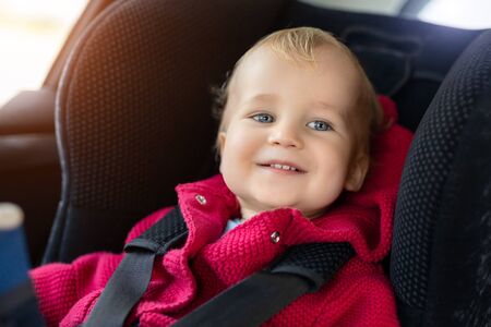 Cute caucasian toodler boy sitting in child safety seat in car during road trip. Adorable baby smiling and enjoying trip in comfortable place in vehicle. Children care and safety on road.の写真素材
