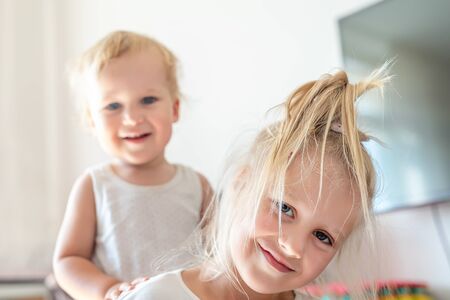 Cute adorable blond caucaian little sister hugging her toddler brother.couple of cheerful sibling playing indoor. Cute girl and baby boy enjoy relaxing at home. Happy childhood, family love, and care.の写真素材
