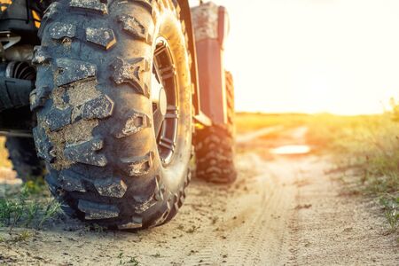 Close-up tail view of ATV quad bike on dirt country road at evening sunset time. Dirty wheel of AWD all-terrain vehicle. Travel and adventure concept.Copyspace.Toned.の写真素材