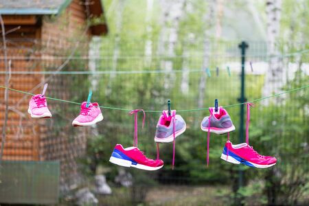 Three pairs of bright sport fitness sneakers hanged on clothespin at backyard after laundry outdoors. Preparartion for running training or marathon.の写真素材